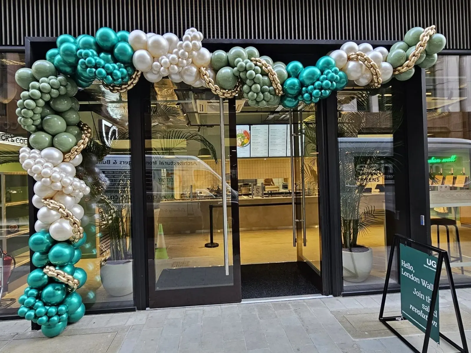 Green, white and teal organic balloon arch installed around a shop entrance